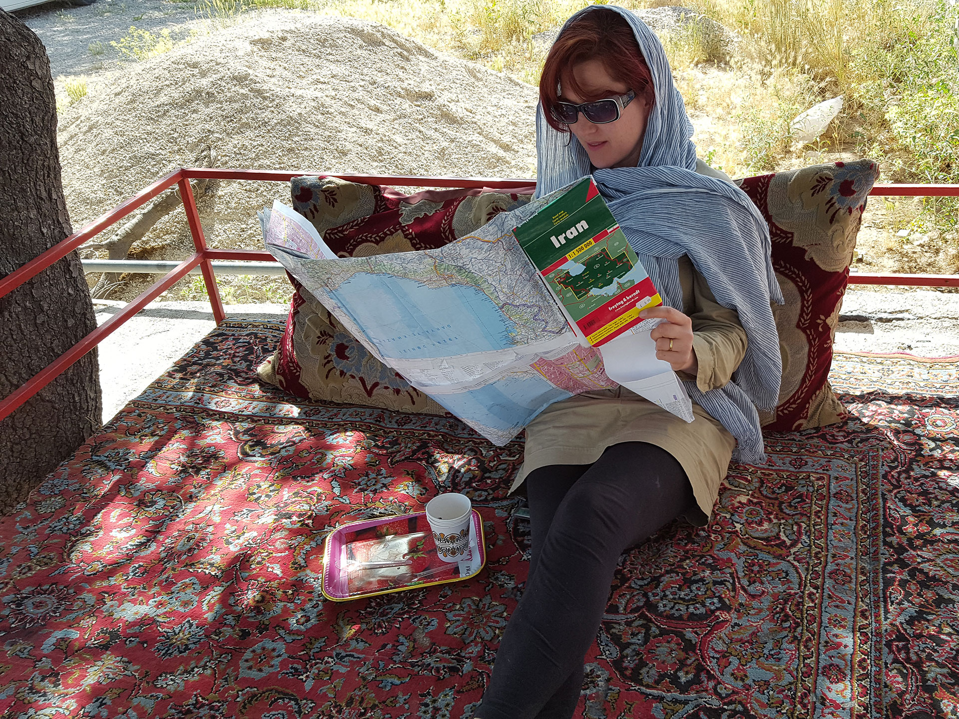 Lois Pryce reclining in the shade reading a map of Iran during her motorcycle adventure