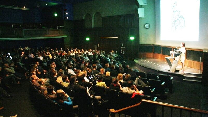 Adventure speaker Lois Pryce talking on stage at the RGS with a large audience