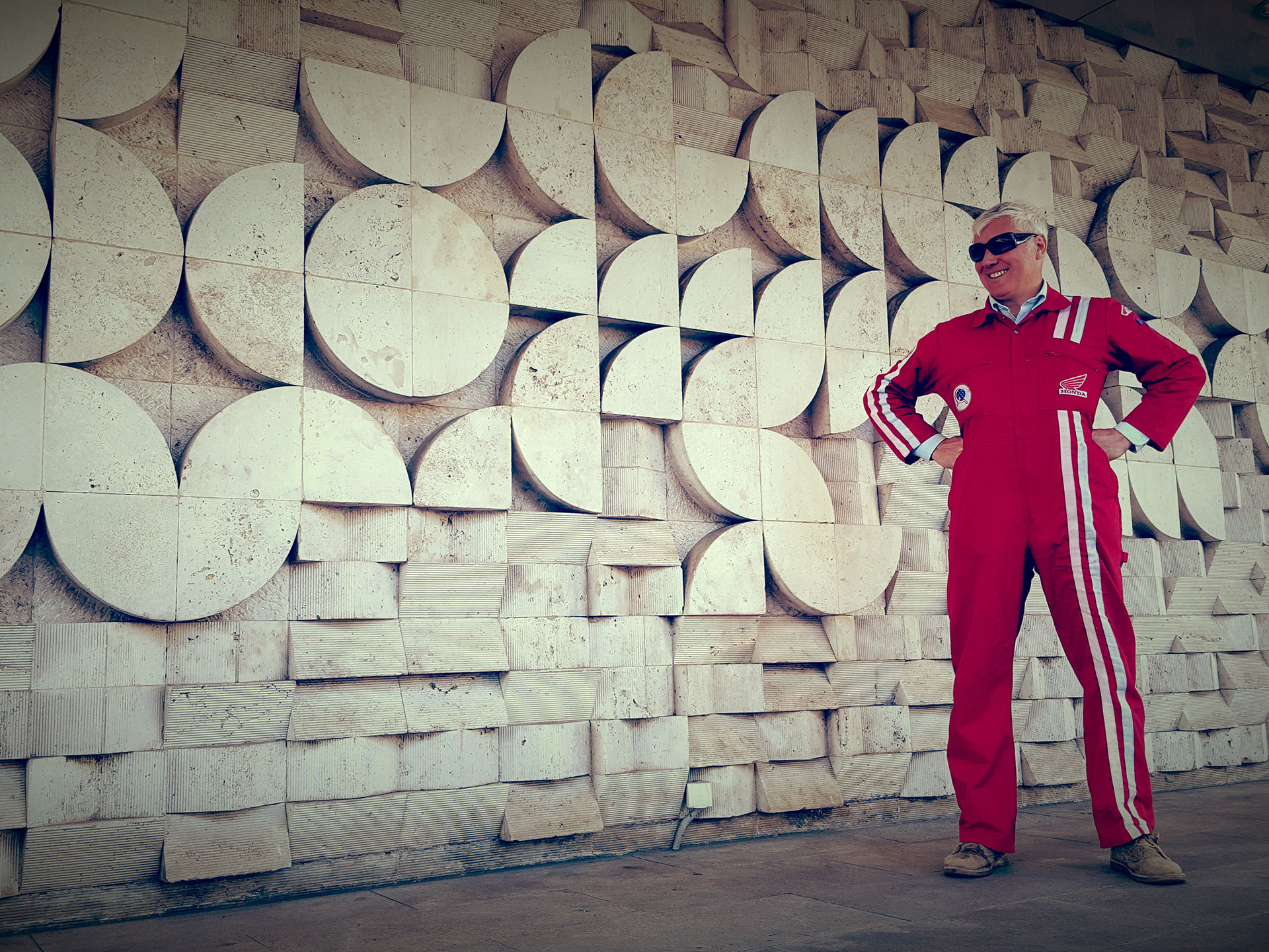 Austin Vince in red overalls by a Socialist Modernist relief tiled mural in Hungary