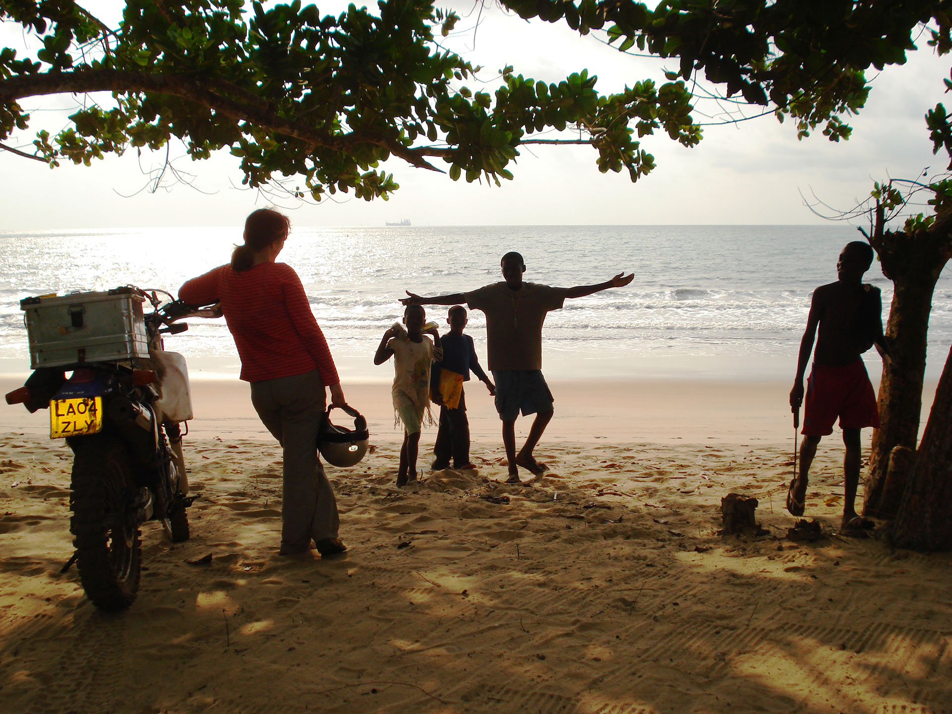 Adventure author Lois Pryce with her motorbike on the beach in Cameroon talking to a group of people