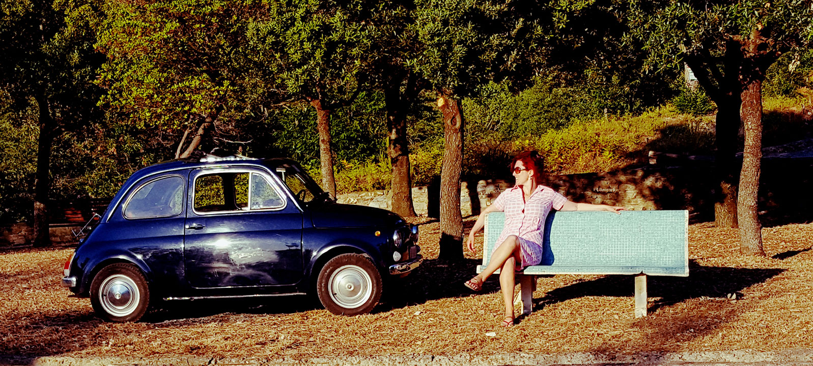 Lois Pryce sitting on a bench by an Italian vintage Fiat car