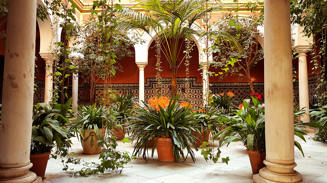 Seville courtyard full of plants with stone columns and colourful tiles