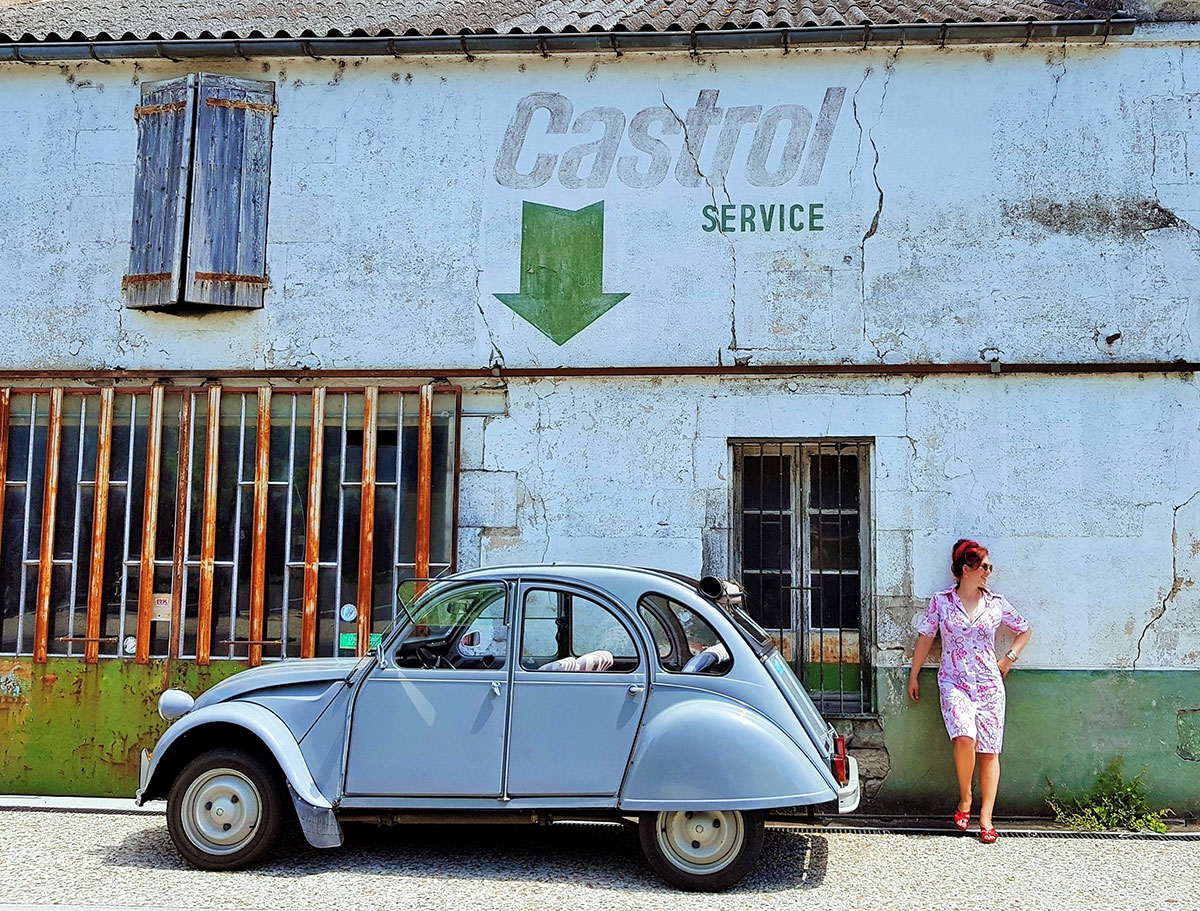 Female adventurer Lois Pryce and a 2CV outside a vintage French garage